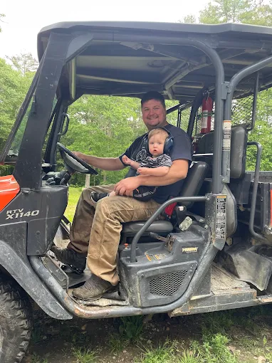Father and baby son sitting together in utility vehicle on farm
