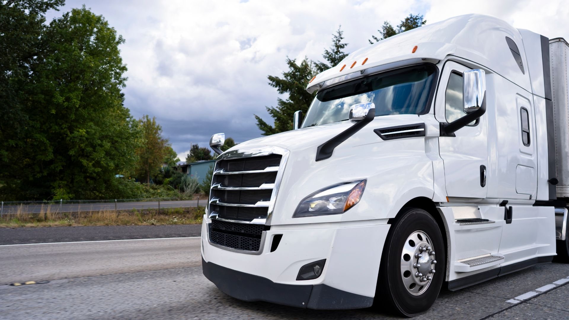 White semi-truck parked on road with trees and cloudy sky